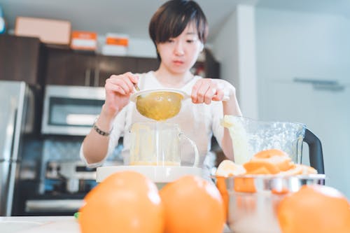 Mujer En Camiseta Blanca Con Cuello Redondo Sosteniendo Un Tazón De Vidrio Transparente Con Frutas Naranjas