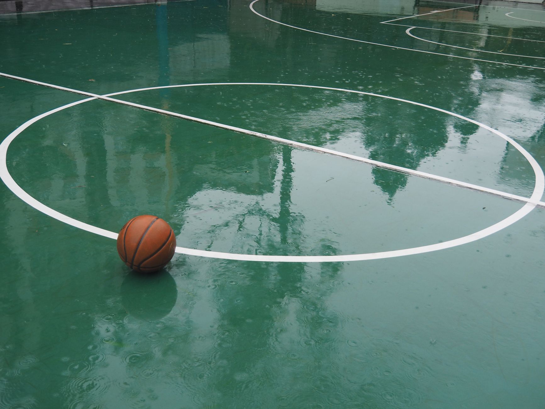 A basketball sits on a rain-soaked court in Hong Kong, reflections visible on the wet surface.