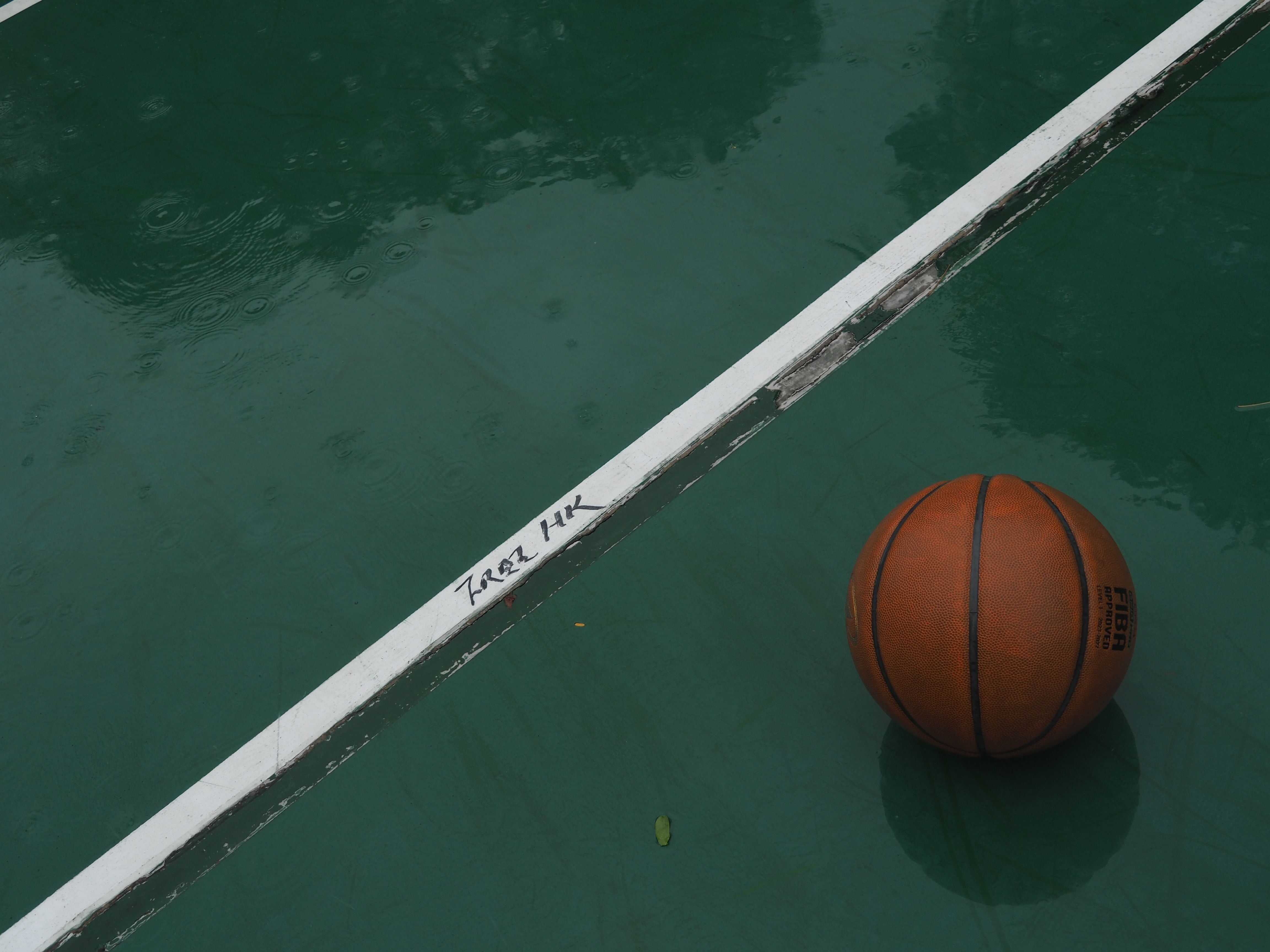 An orange basketball rests on a rain-soaked green court in Hong Kong, adding a moody urban vibe.