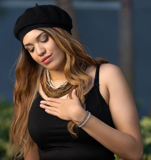 Free A woman in a black beret with layered necklaces, outdoors, gently holding her chest in reflection. Stock Photo