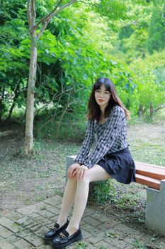 A young woman sits on a park bench surrounded by lush greenery on a summer day in Nanjing, China.
