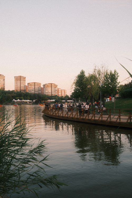 Free Tranquil lakeside walkway with city skyline at sunset, reflecting in water. Stock Photo