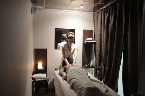 Professional masseuse in white uniform massaging shoulders and neck of relaxed female client while working in comfortable modern salon