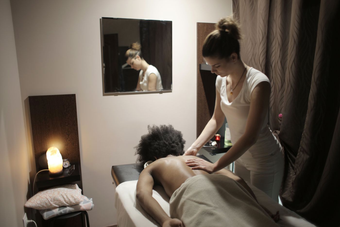 Professional therapist massaging the back of an African woman in a modern spa