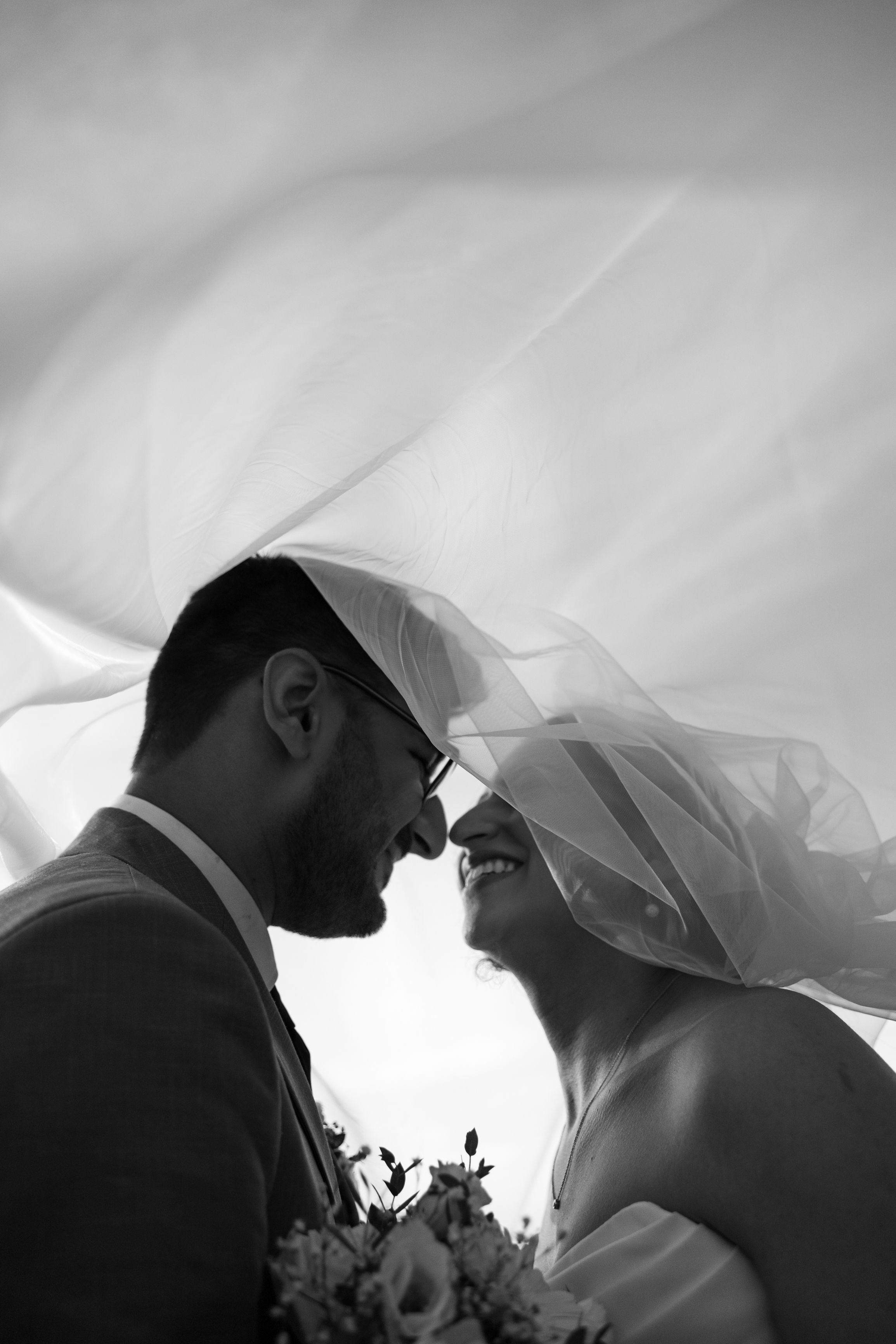 Elegant black and white wedding photo capturing a tender moment under a veil.