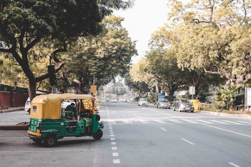 Old green auto rickshaw turning at intersection on street near lush tropical trees on sunny day