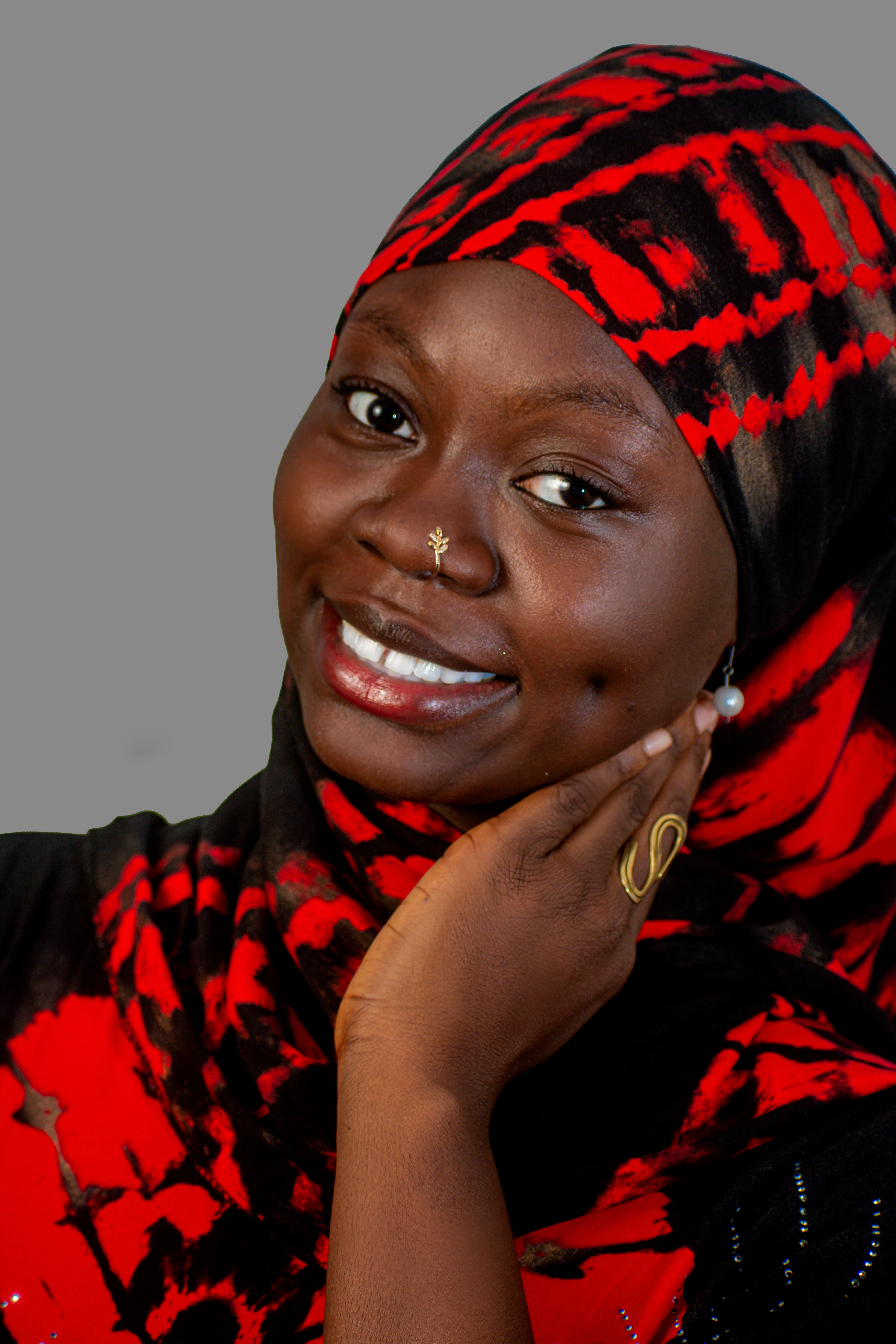 Vibrant portrait of a smiling woman wearing a red and black hijab with gold jewelry, exuding warmth and confidence.
