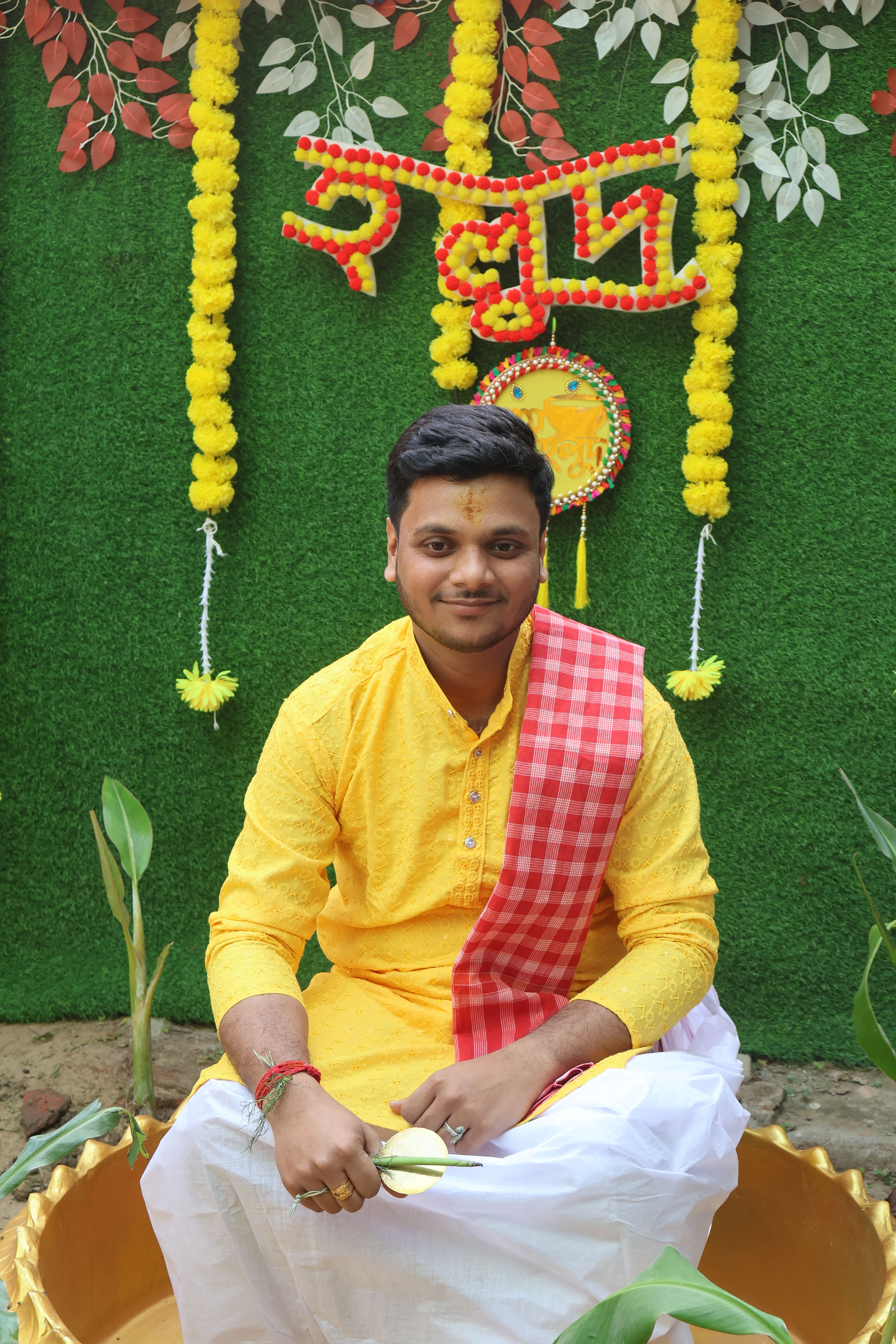 A young man in traditional Indian attire smiles amidst vibrant decorations, celebrating a cultural event.