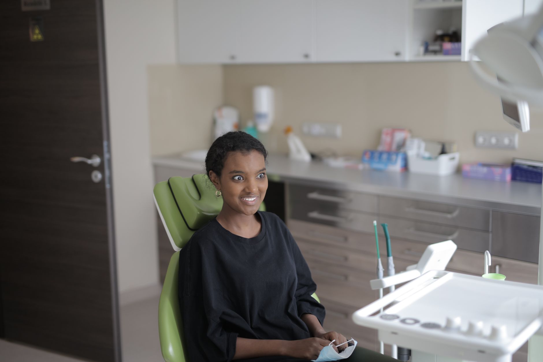 Surprised young ethnic female client in black casual clothes sitting in dental chair and looking away before treating te