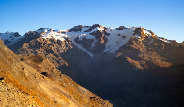 Breathtaking view of snow-capped Alps under clear blue sky during sunrise.