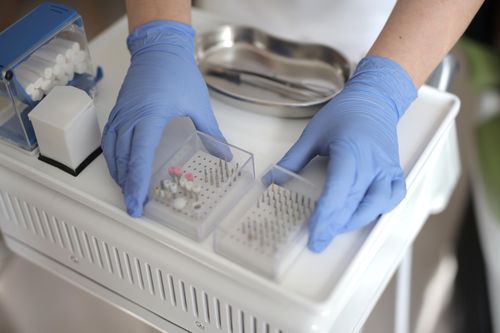 Free From above view of crop unrecognizable medical specialist in latex gloves holding plastic containers with metal heads of dental drill during work in modern clinic Stock Photo