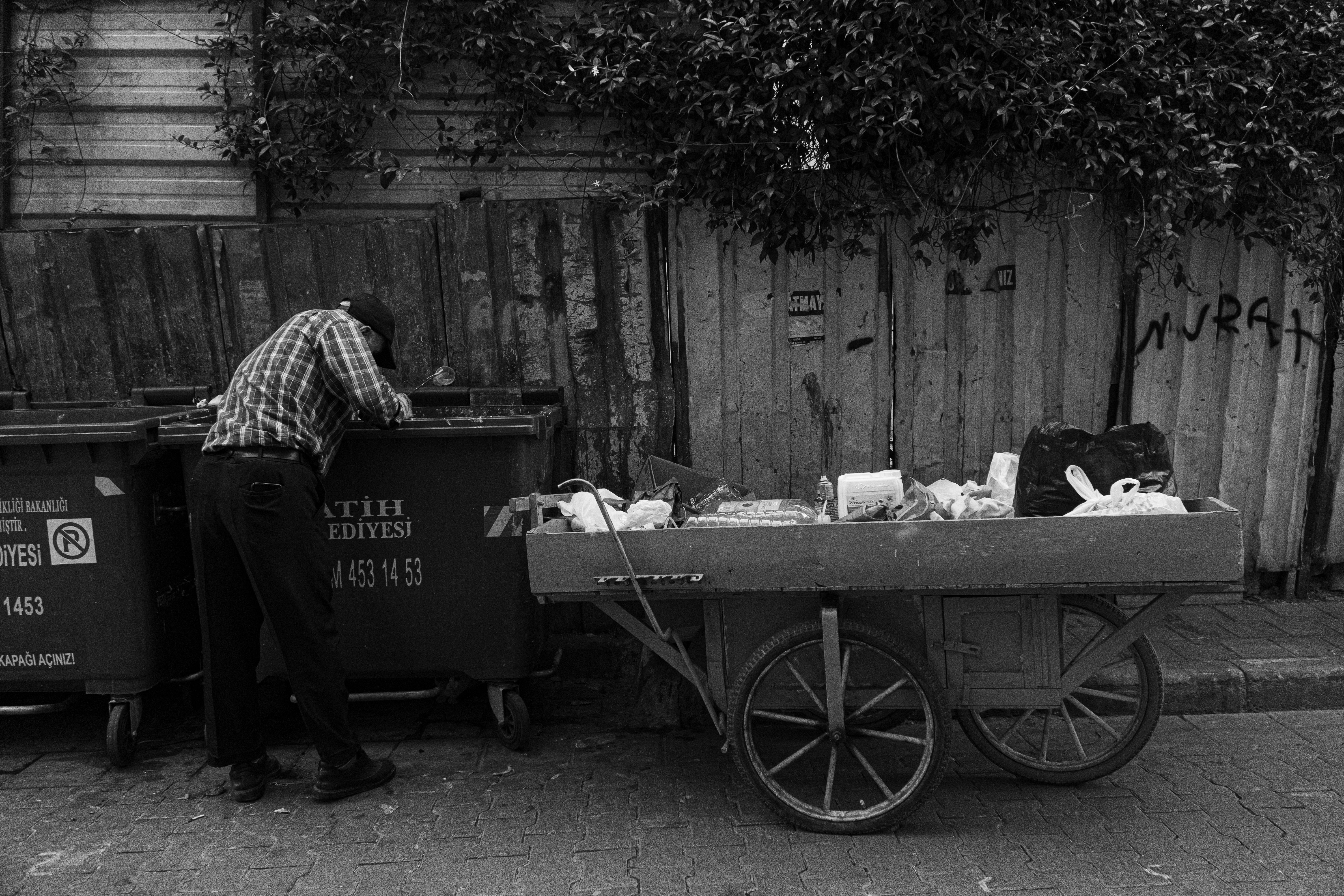 A poignant black and white street photograph depicting a man searching through trash in Istanbul, Türkiye.
