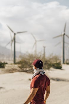 一个人站在沙漠中，观察着多台风力涡轮机，展现了可再生能源的景象