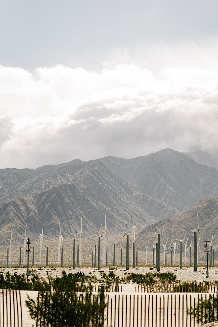 Wind Turbines In Mountainous Valley Against Cloudy Sky