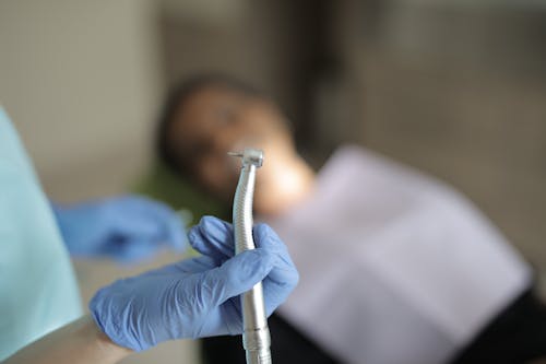 Unrecognizable crop dentist in latex gloves holding dental drill in hand while treating teeth of patient in modern clinic