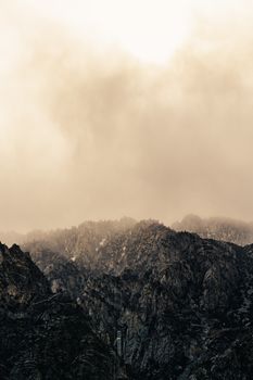Breathtaking landscape of rocky mountains under misty clouds floating over high peaks on overcast day