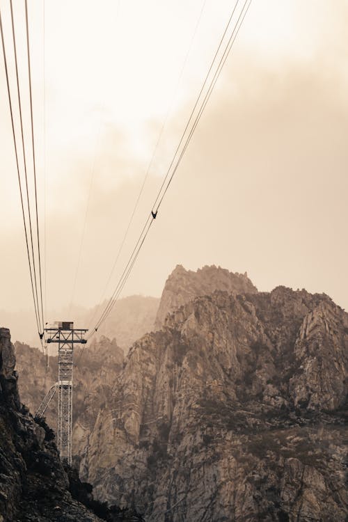 From below of cable railway in breathtaking high rocky mountains against cloudy sky