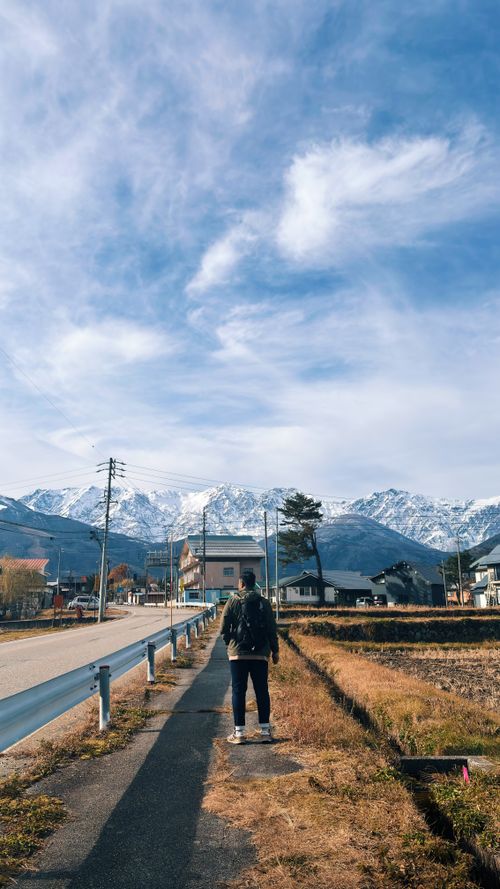 Free A person walks towards the snow-capped Japanese Alps under a bright blue sky. Stock Photo