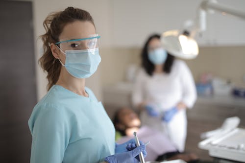Young female dentist in medical uniform with instruments standing in clinic