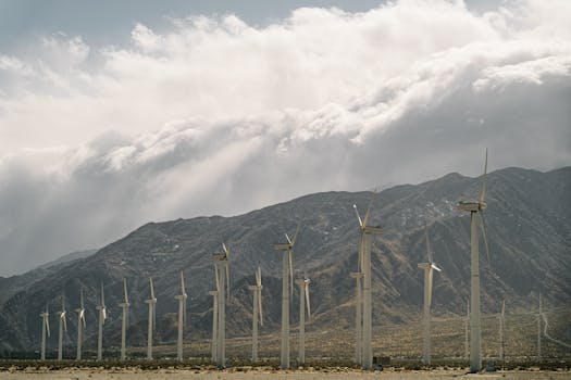 A row of wind turbines set before majestic mountains and a cloudy sky, emphasizing sustainable energy.