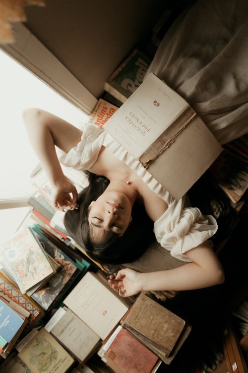 Free Woman relaxing with a book in a cozy, vintage-style nook filled with literature. Stock Photo