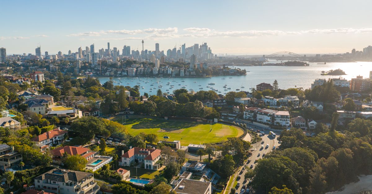 A vibrant aerial shot of Sydney, showcasing the skyline, harbor, and iconic Harbor Bridge under a clear blue sky.