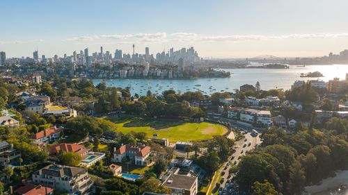 Free A vibrant aerial shot of Sydney, showcasing the skyline, harbor, and iconic Harbor Bridge under a clear blue sky. Stock Photo