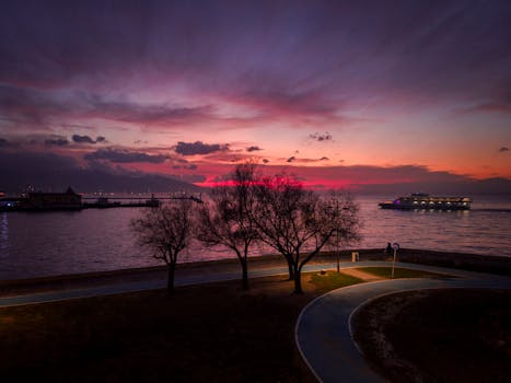 Picturesque purple sunset sky reflecting in calm sea water with floating modern vessel near well groomed embankment