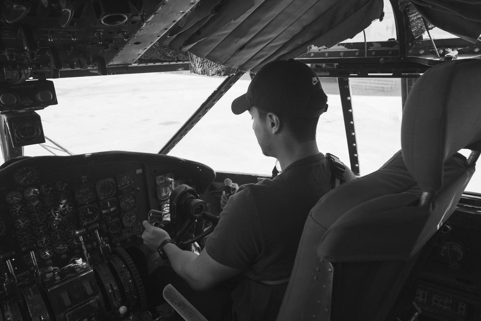 Monochrome photo of a pilot in an airplane cockpit, focusing on aviation controls.