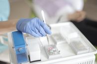 Anonymous medical specialist in latex gloves using forceps to take detail from plastic container while working in modern clinic