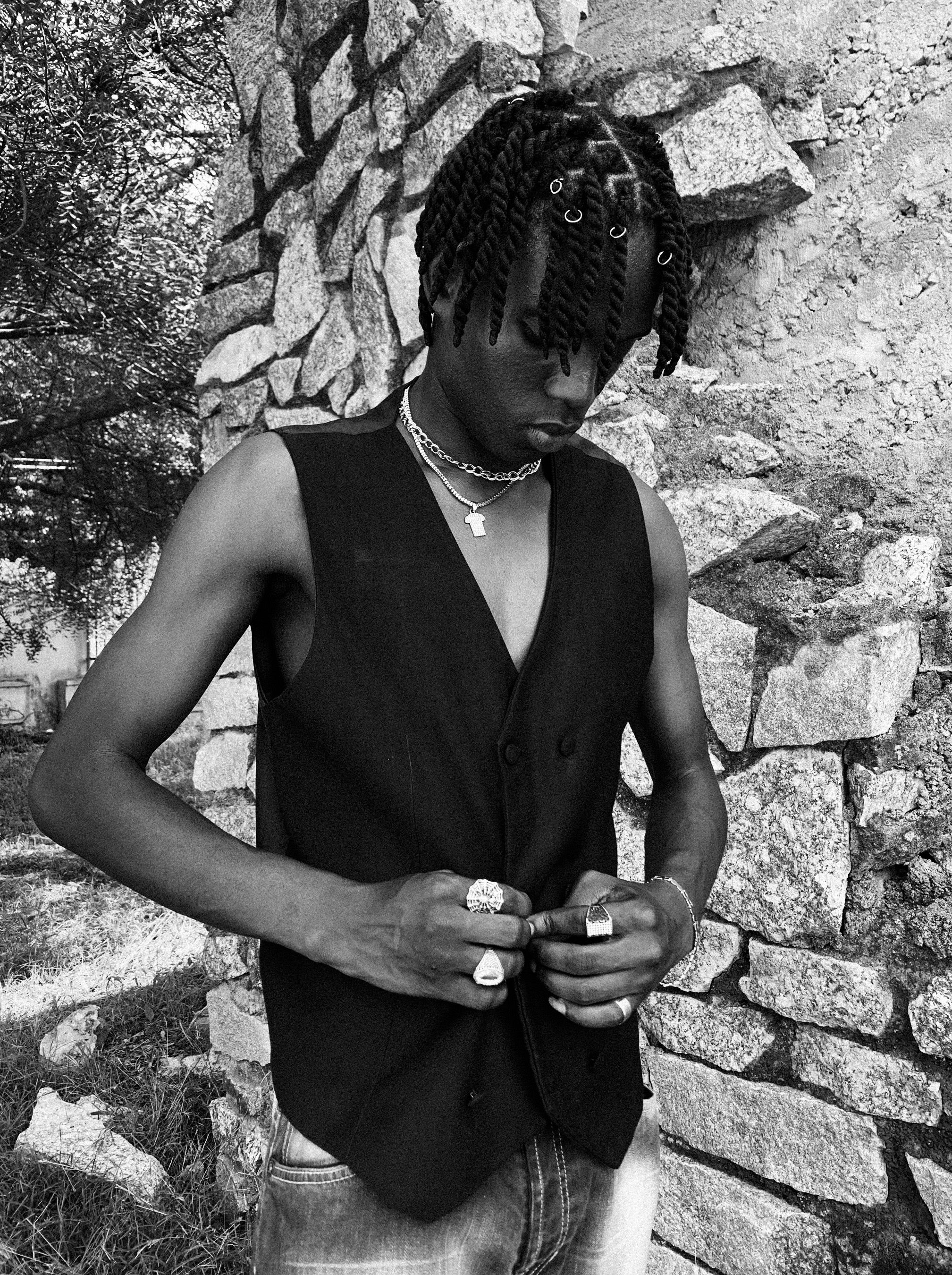 Portrait of a stylish young man wearing a black vest, standing next to a stone wall in Zaria, Nigeria.