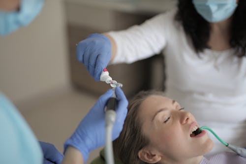 Unrecognizable crop dentists in latex gloves and masks working with professional equipment while treating teeth of patient in modern dental clinic