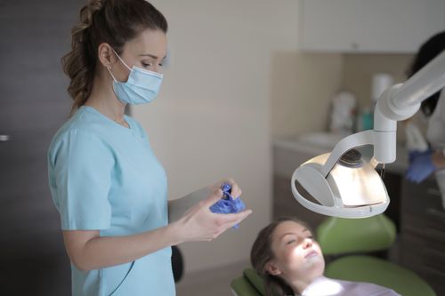 Free Side view of young female dentist in medical mask and uniform taking off latex gloves after treatment patient in modern dental room in clinic Stock Photo