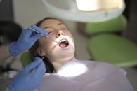 Unrecognizable crop dentist in latex gloves examining teeth of patient in clinic