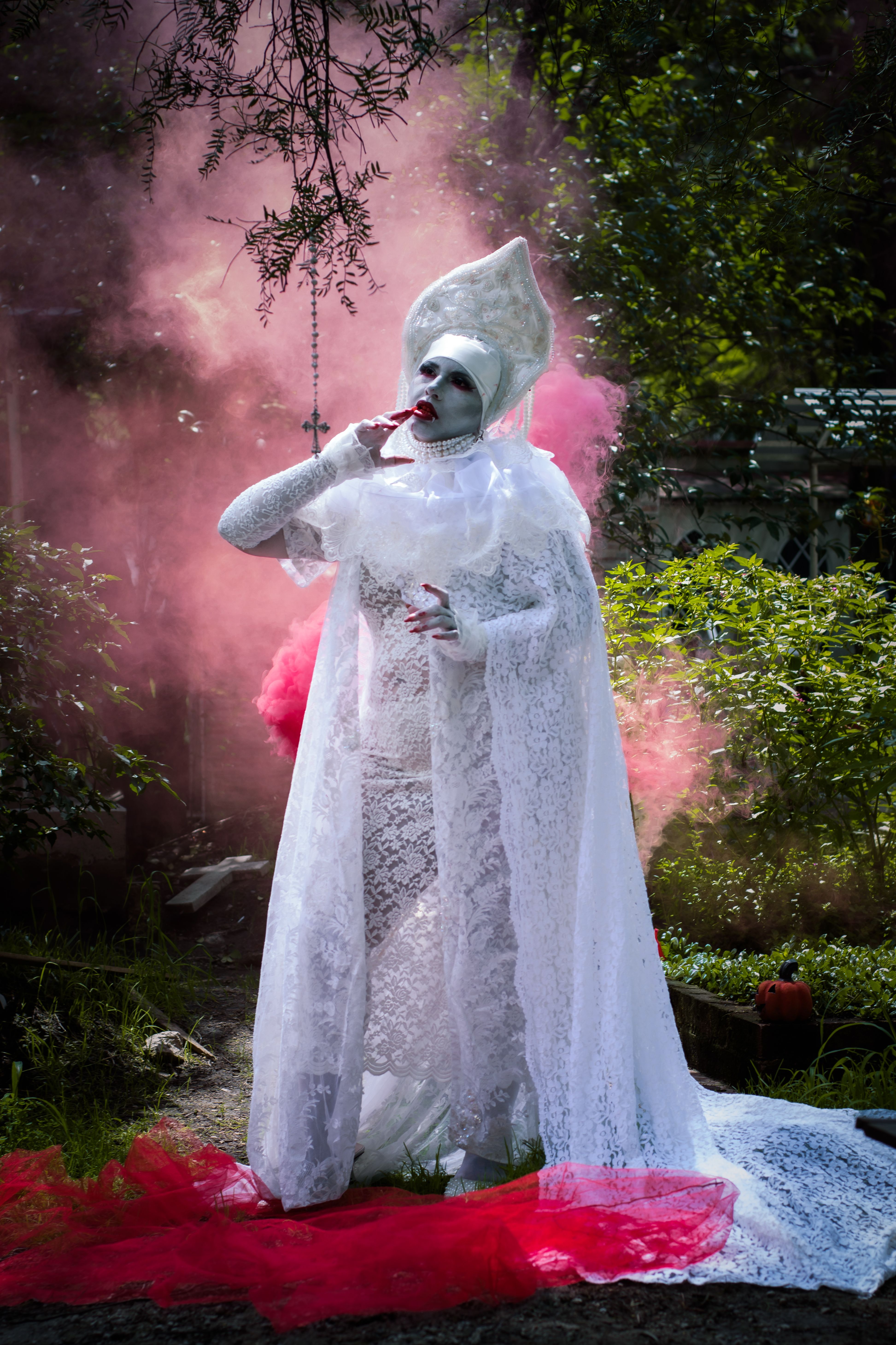 Enchanting figure in ornate white lace robe set against a vibrant smoky background outdoors.