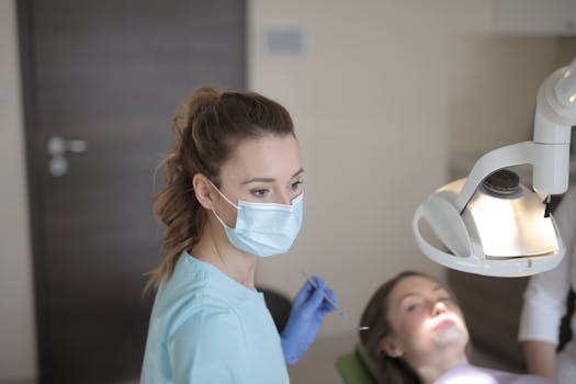 Dentist with face mask examining patient's teeth in a clinic setting.