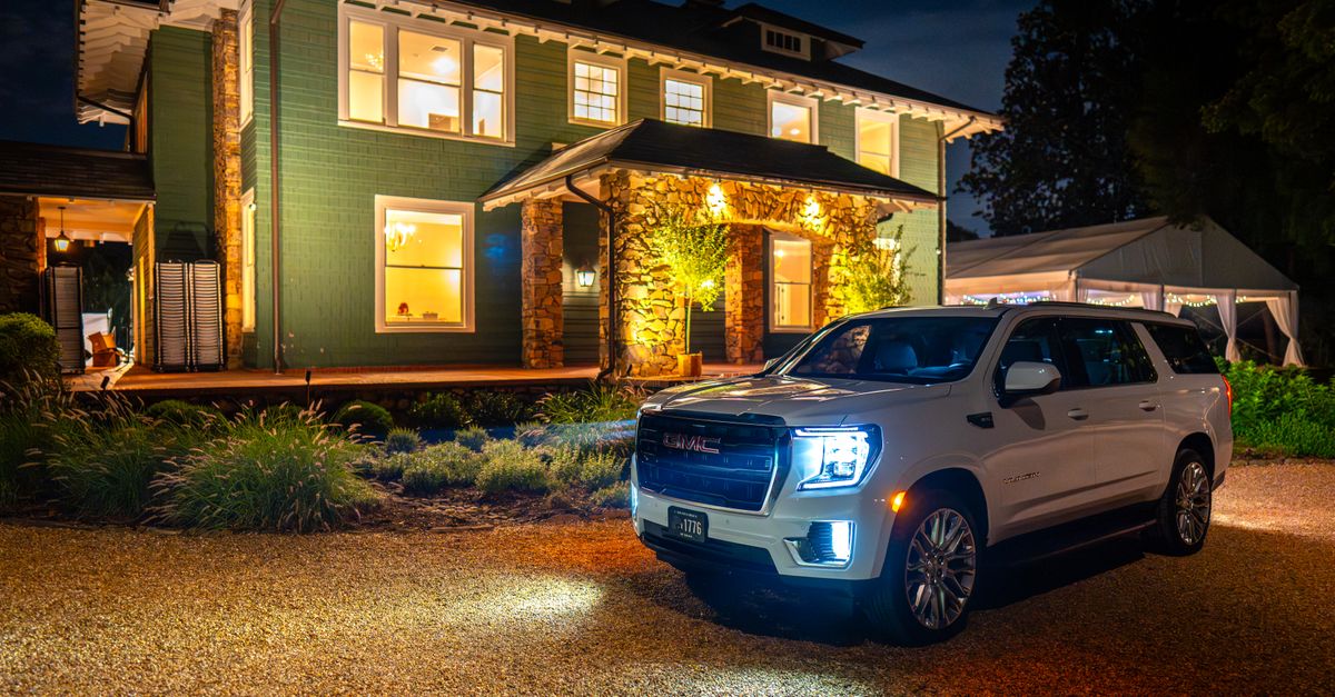 A white luxury SUV parked in front of an illuminated mansion at night in Charlotte.