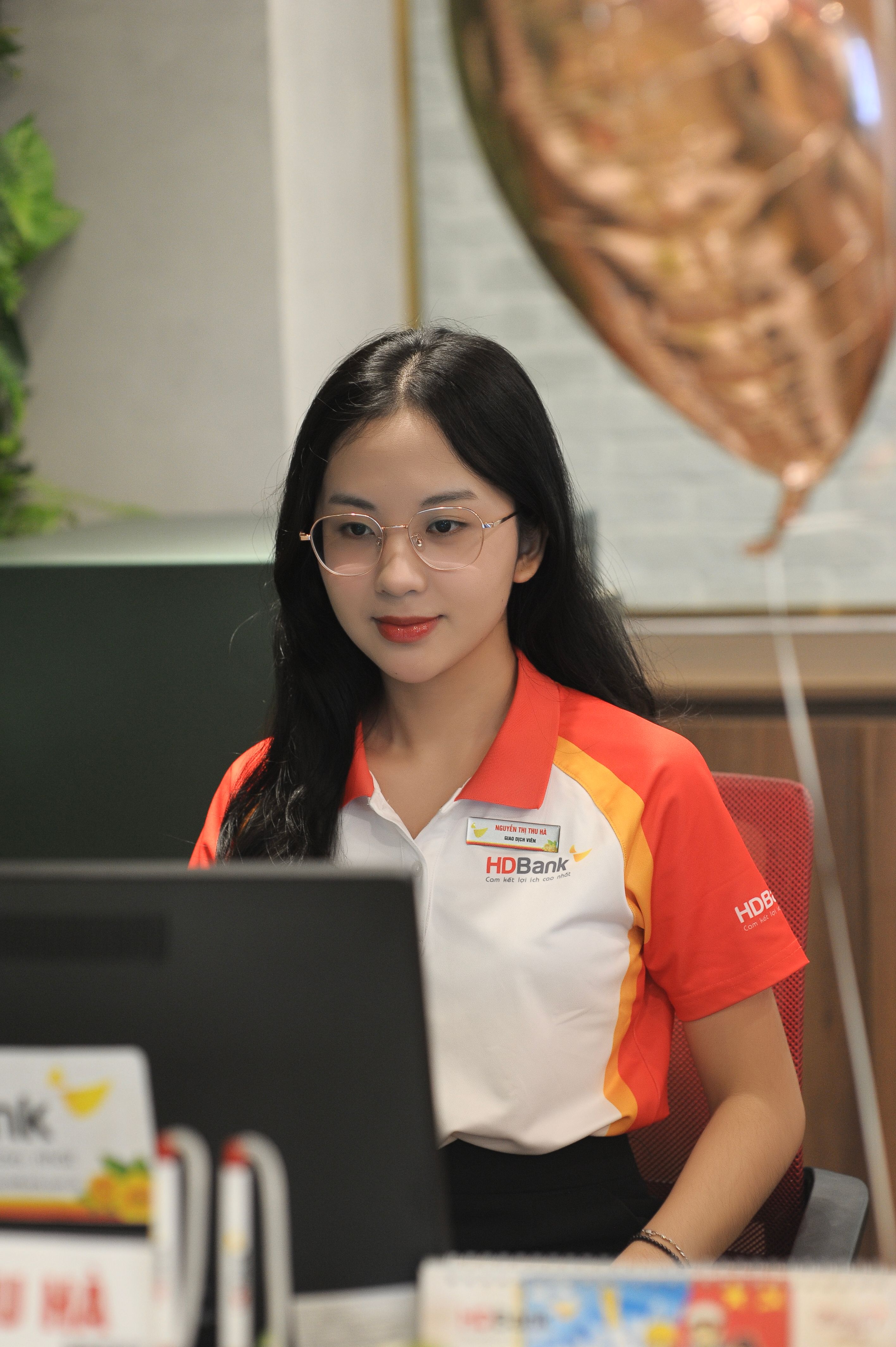 Bank teller in uniform at desk assisting customers, creating a friendly atmosphere.