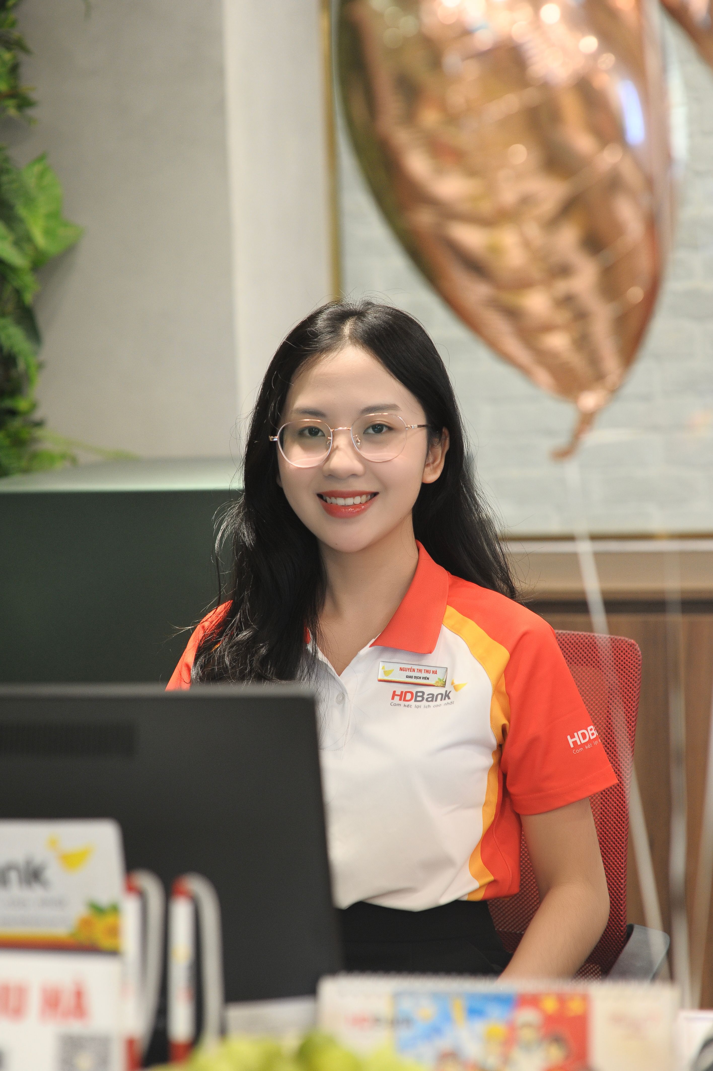 Professional bank employee smiling at her desk with a festive balloon in an office setting.