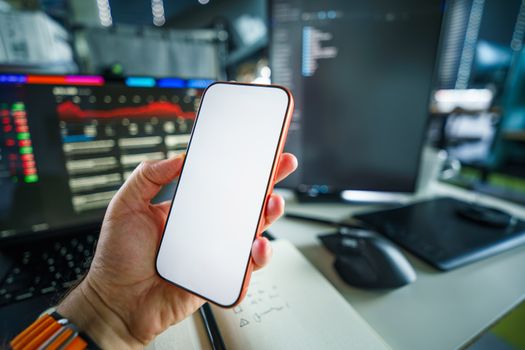 A person holding a smartphone with a blank screen, set within a modern tech office with charts.