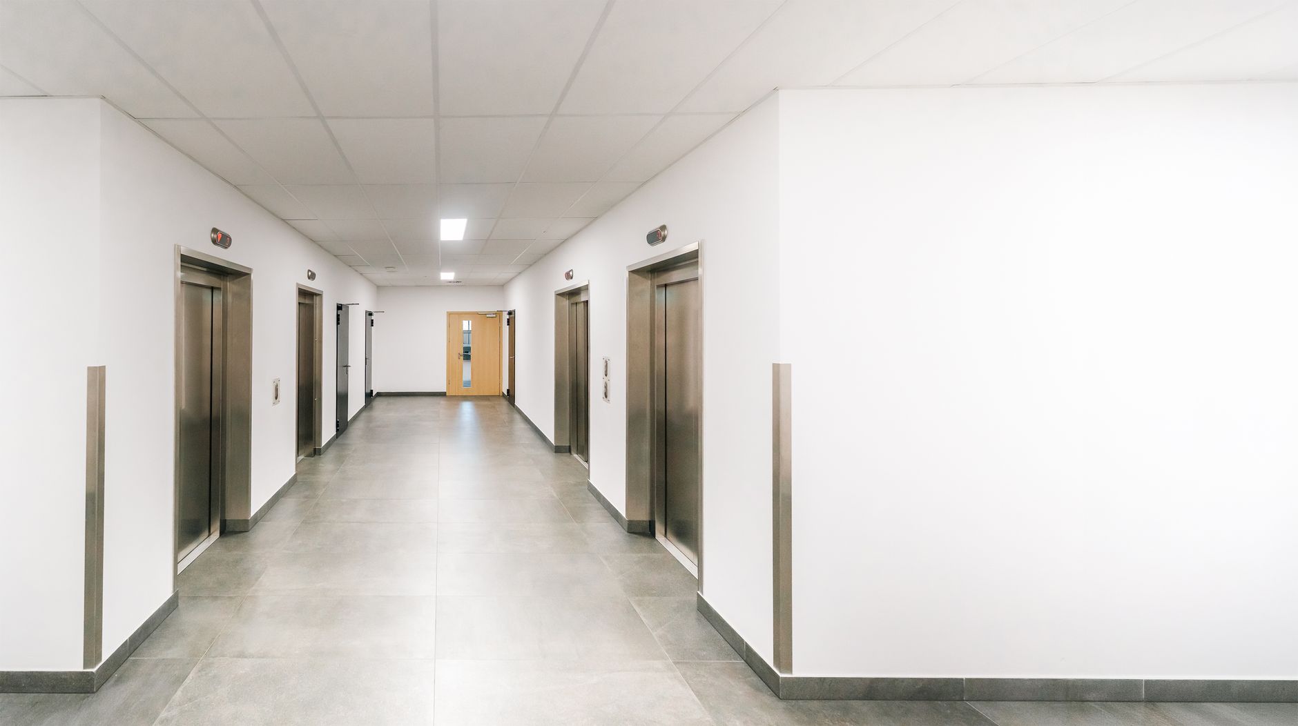 Bright, clean office corridor featuring several modern stainless steel elevators.