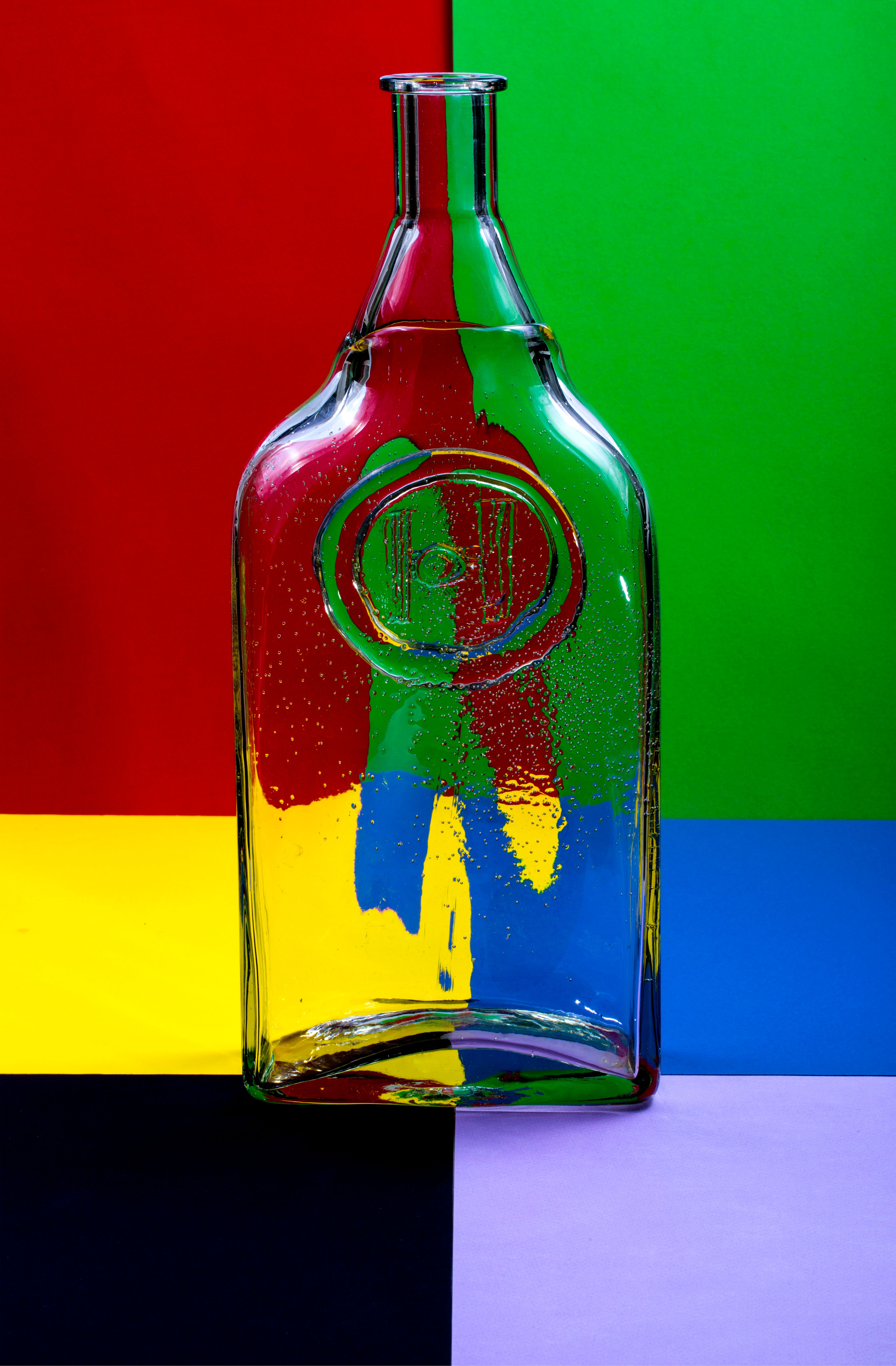 A transparent glass bottle contrasts vividly against a bold multicolored backdrop.