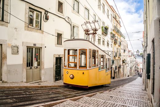 Classic yellow tram on a picturesque street in Lisbon, Portugal, showcasing urban charm and historic architecture.