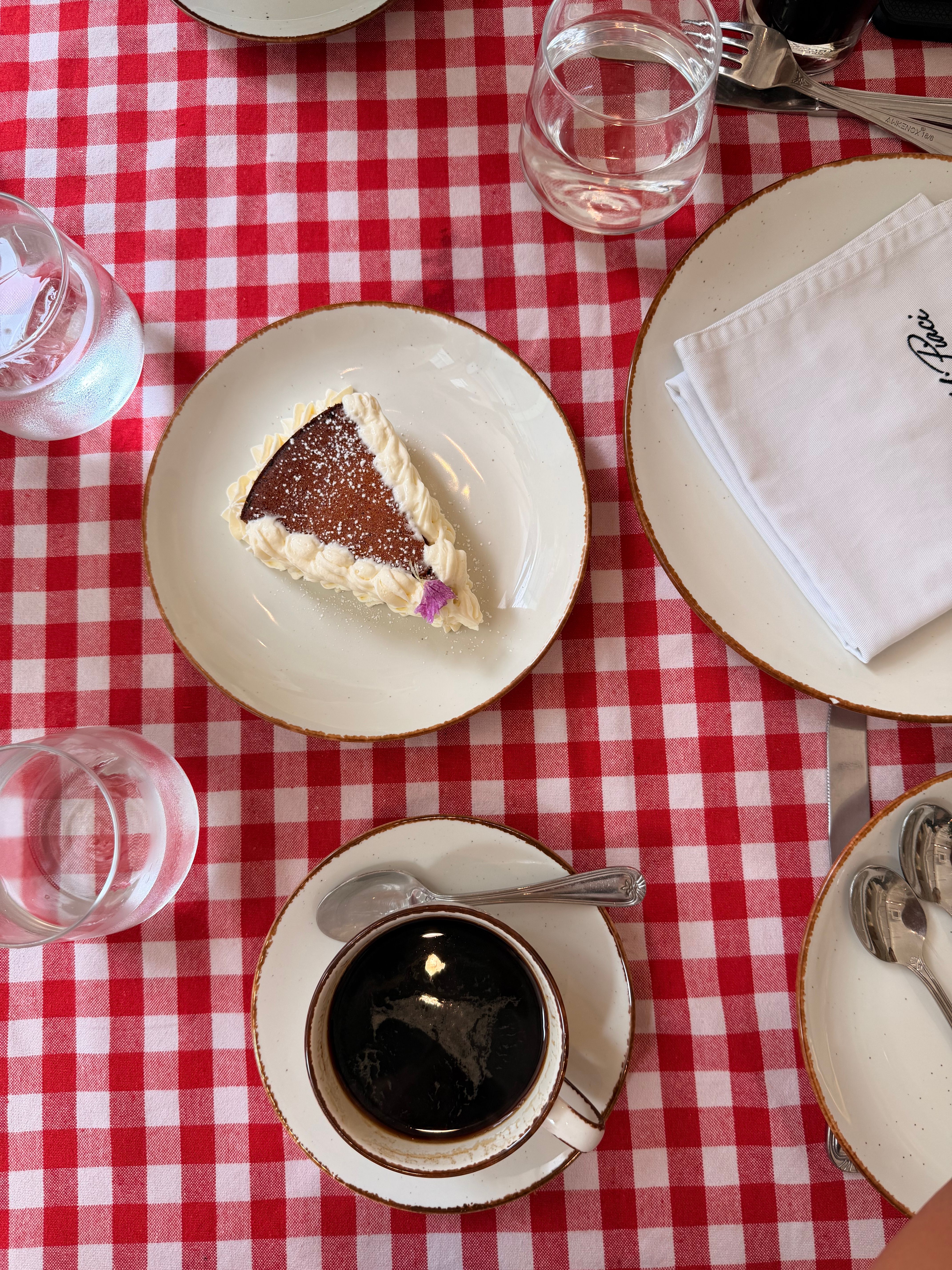 A slice of cake and a cup of coffee on a red checkered tablecloth, creating a cozy cafe vibe.