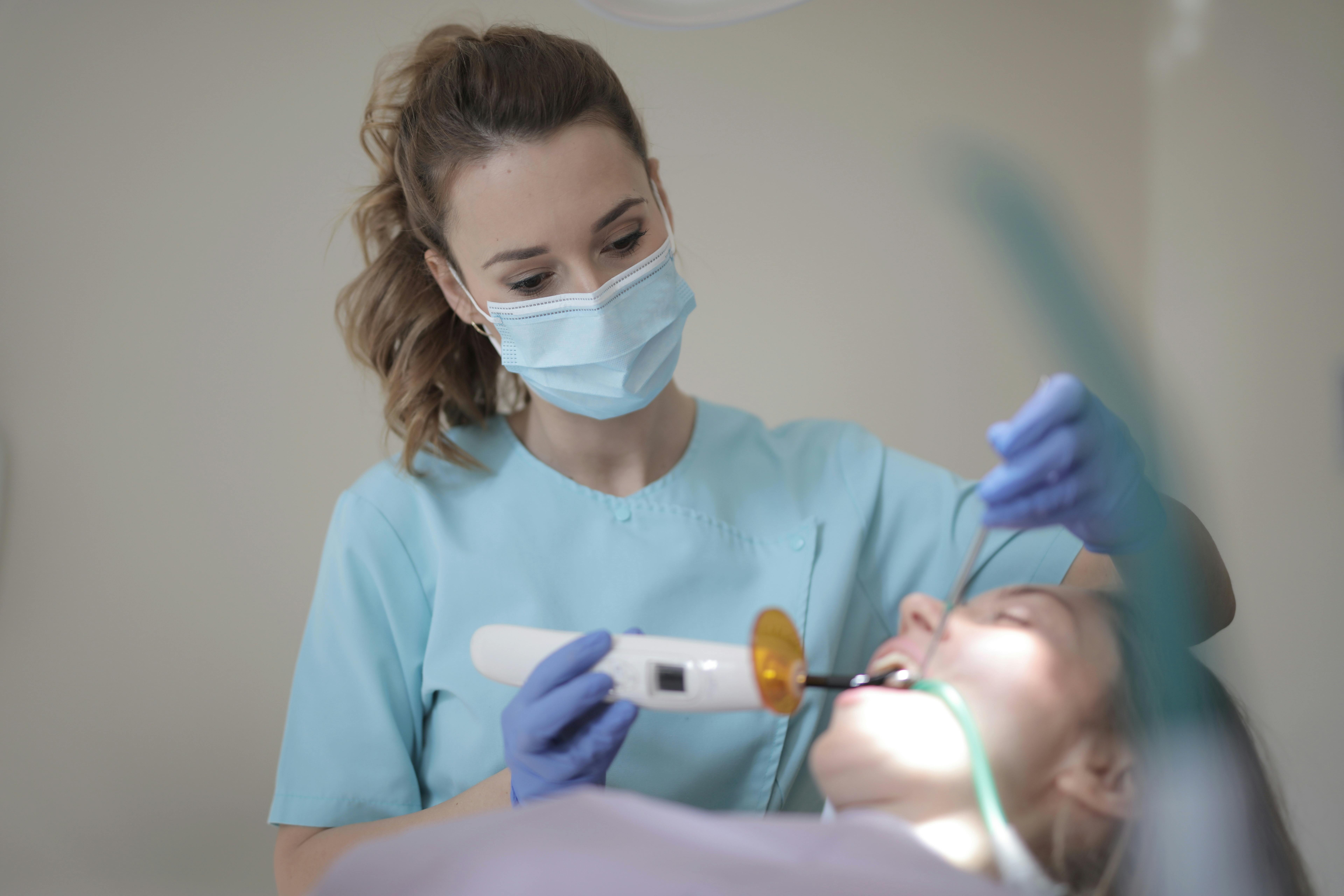 Young female dentist treating teeth of patient with instruments in ...