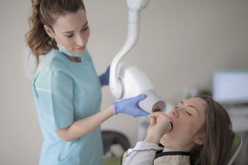 Young female dentist using modern medical equipment while working with patient in clinic