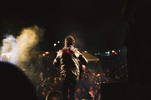 Dynamic view of a musician playing guitar on stage with an engaged crowd during a live concert.