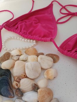 A pink bikini top with seashells and a pearl necklace, exuding a summery beach vibe.