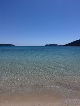 Experience the serene beauty of a Sardinian beach with clear azure waters under a bright summer sky.