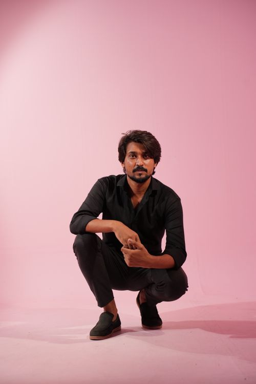 Free Confident man squatting on a pink backdrop, wearing black clothes, exuding style. Stock Photo
